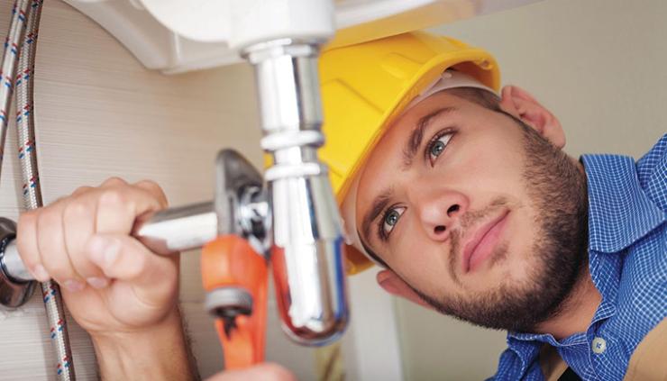 Young man with beard in yellow hard hat tightening sink pipe with wrench