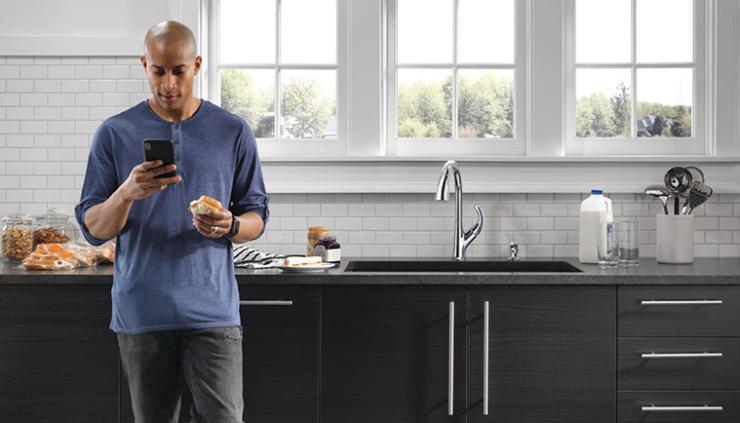 Man wearing blue shirt in modern kitchen looking at phone in front of kitchen counter