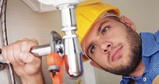Young man with beard in yellow hard hat tightening sink pipe with wrench