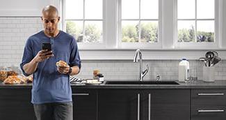 Man wearing blue shirt in modern kitchen looking at phone in front of kitchen counter